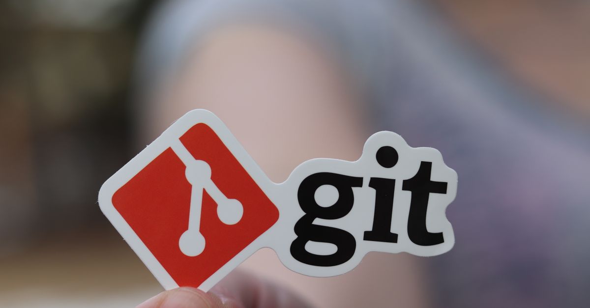 Close-up of a person holding a Git sticker, emphasizing software development.